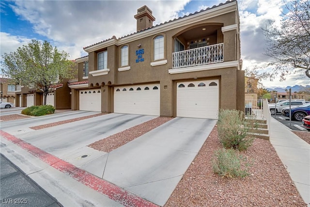 view of front facade featuring concrete driveway, a balcony, a chimney, an attached garage, and stucco siding