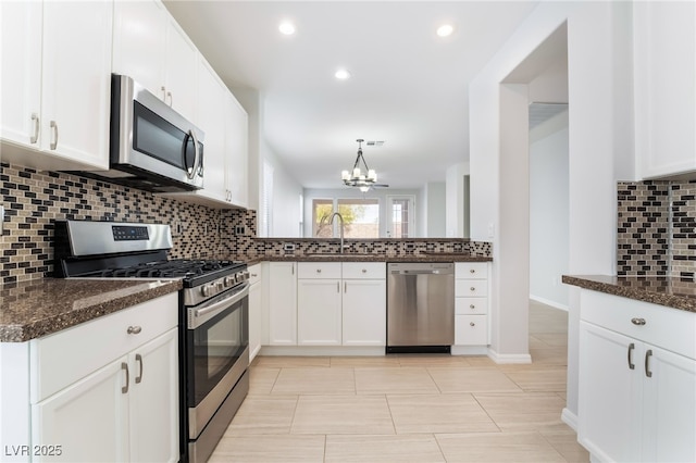 kitchen featuring tasteful backsplash, appliances with stainless steel finishes, white cabinetry, a sink, and dark stone countertops