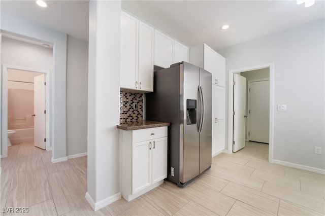 kitchen with dark countertops, tasteful backsplash, stainless steel refrigerator with ice dispenser, and white cabinetry