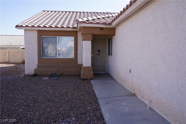 doorway to property featuring stucco siding, fence, and a tiled roof