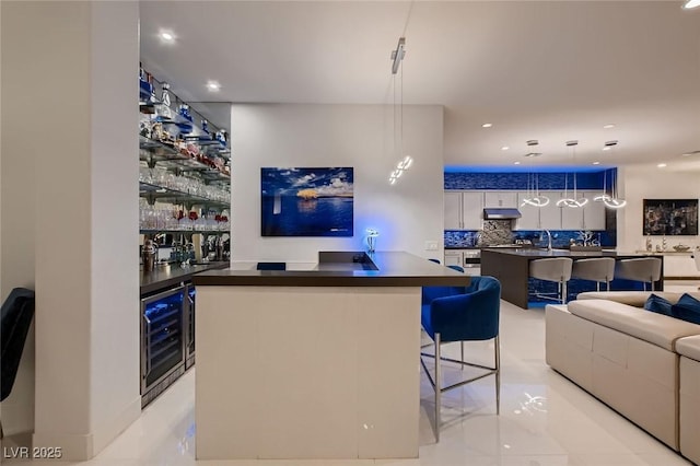 bar featuring under cabinet range hood, beverage cooler, hanging light fixtures, decorative backsplash, and wet bar