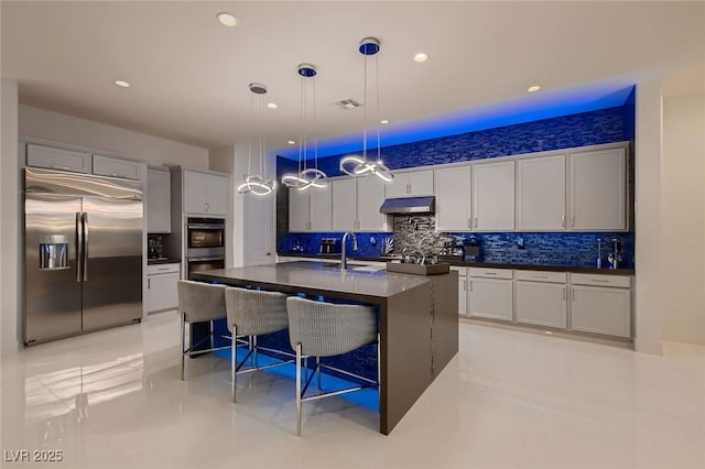 kitchen with a breakfast bar area, under cabinet range hood, visible vents, appliances with stainless steel finishes, and dark countertops