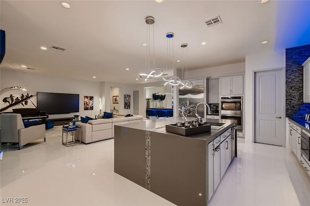 kitchen featuring visible vents, dark countertops, a kitchen island with sink, double oven, and a sink