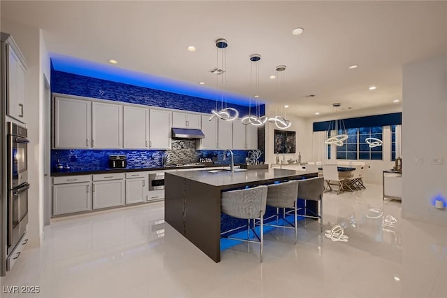 kitchen with a breakfast bar, appliances with stainless steel finishes, decorative backsplash, dark countertops, and decorative light fixtures