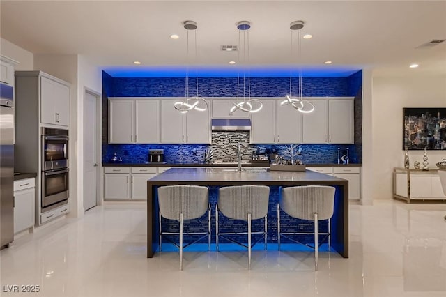 kitchen featuring visible vents, dark countertops, stainless steel appliances, under cabinet range hood, and a sink