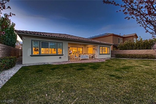 back of house at dusk featuring a patio, a yard, fence, and stucco siding