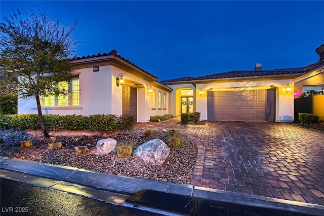 mediterranean / spanish-style house featuring a tiled roof, decorative driveway, an attached garage, and stucco siding