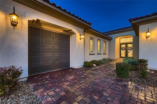 property entrance with french doors, an attached garage, a tile roof, and stucco siding