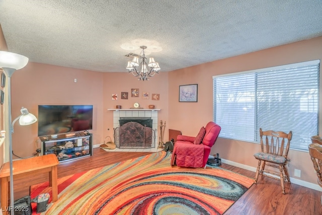 living room featuring baseboards, wood finished floors, a textured ceiling, a fireplace, and a chandelier