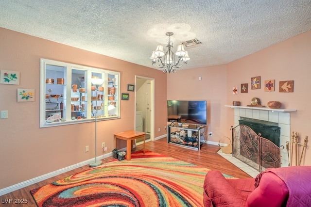 living area with a chandelier, visible vents, a tiled fireplace, and wood finished floors