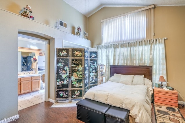 bedroom with visible vents, vaulted ceiling, ensuite bathroom, and wood finished floors