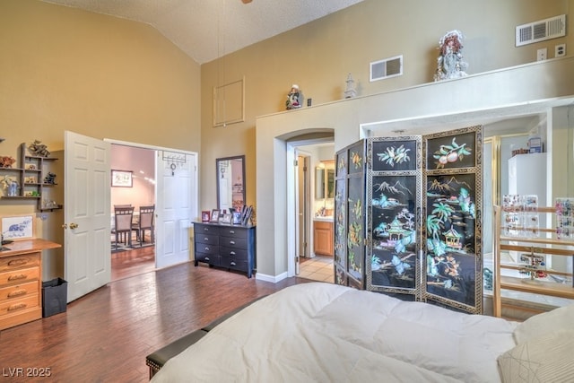 bedroom featuring high vaulted ceiling, visible vents, arched walkways, and wood finished floors