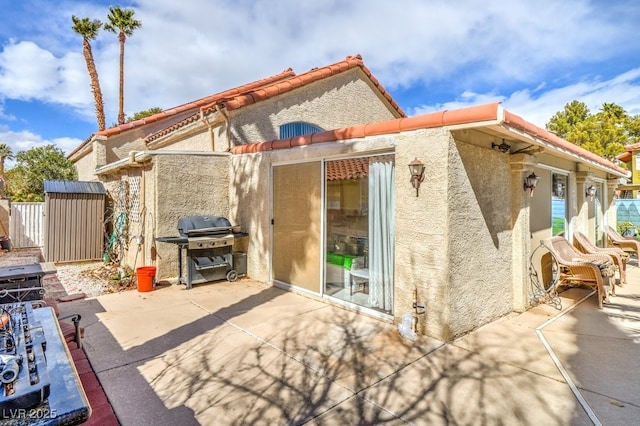 back of house featuring a tile roof, stucco siding, a patio area, a shed, and an outdoor structure