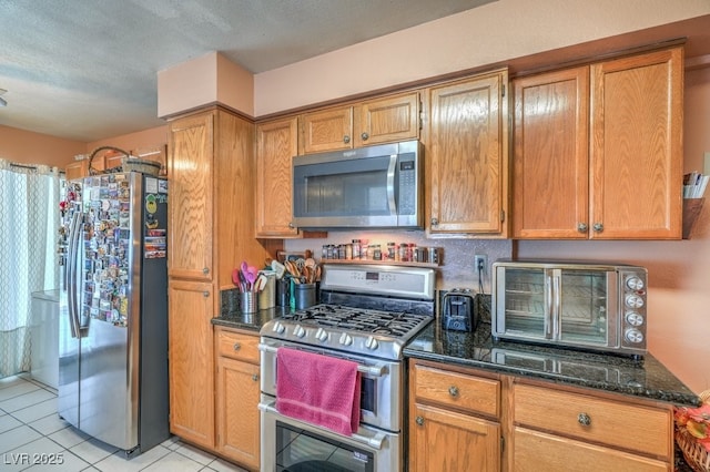 kitchen featuring a toaster, light tile patterned floors, stainless steel appliances, brown cabinetry, and dark stone counters