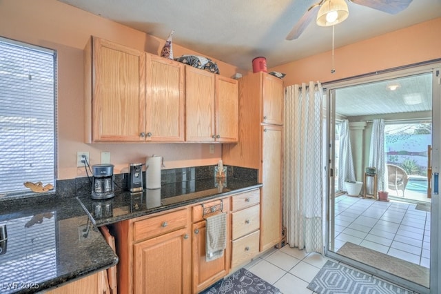 kitchen with light tile patterned floors, ceiling fan, light brown cabinets, and dark stone countertops