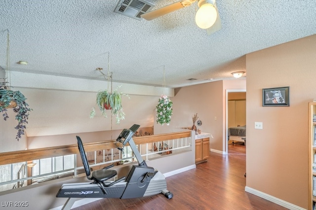 workout area featuring a textured ceiling, ceiling fan, wood finished floors, visible vents, and baseboards