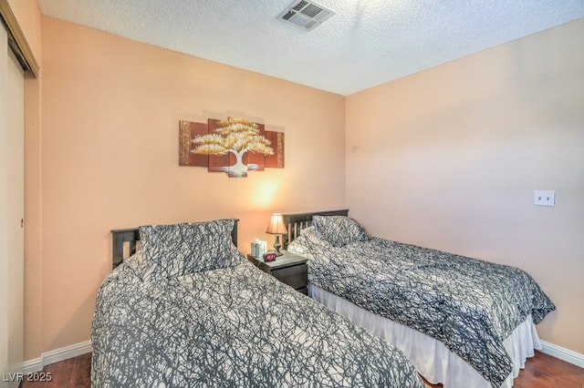 bedroom featuring a textured ceiling, wood finished floors, visible vents, and baseboards