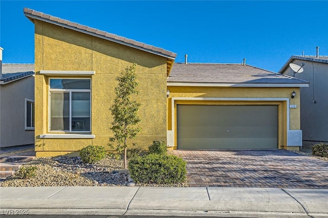 view of front of house featuring stucco siding, a tiled roof, decorative driveway, and a garage