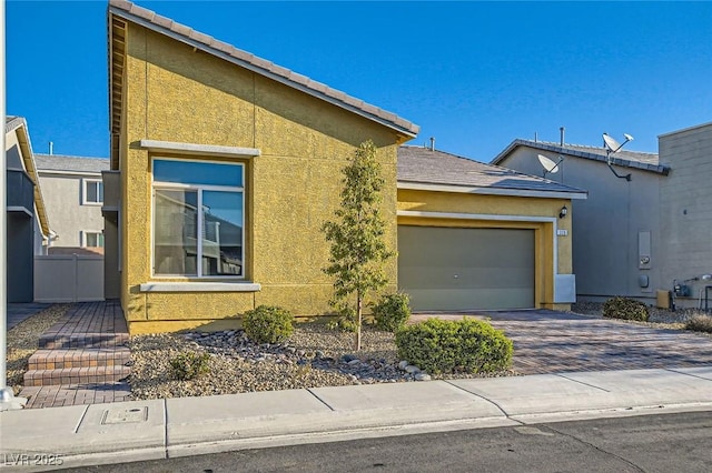 view of front facade featuring decorative driveway, fence, an attached garage, and stucco siding