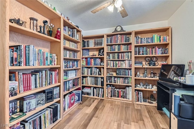 living area with wall of books, ceiling fan, a textured ceiling, and wood finished floors