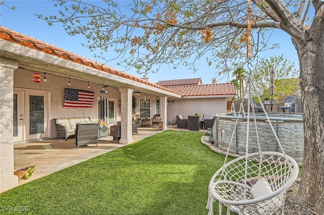 back of house with stucco siding, a lawn, an outdoor hangout area, a patio area, and a tiled roof