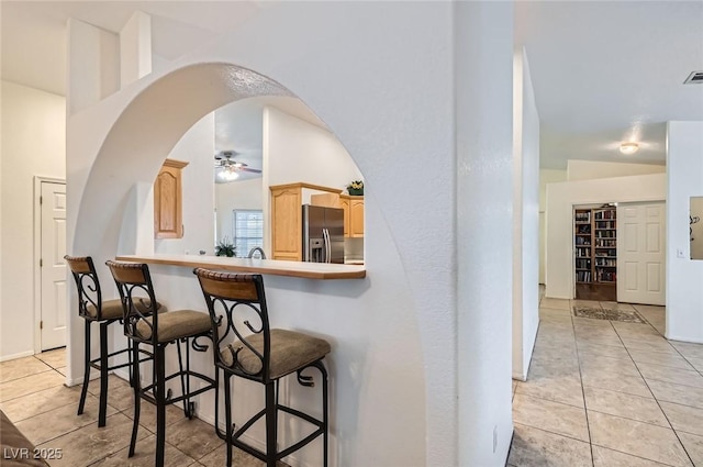 kitchen featuring arched walkways, a kitchen breakfast bar, stainless steel fridge with ice dispenser, and light tile patterned floors