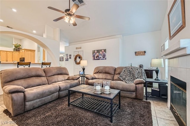 living area featuring arched walkways, a fireplace, visible vents, a ceiling fan, and high vaulted ceiling