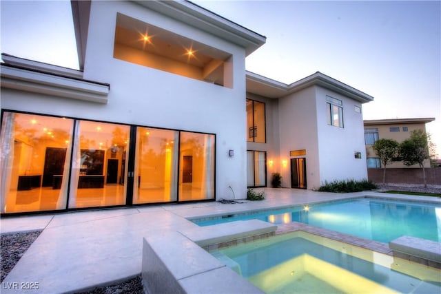 rear view of property with a patio area, a pool with connected hot tub, and stucco siding