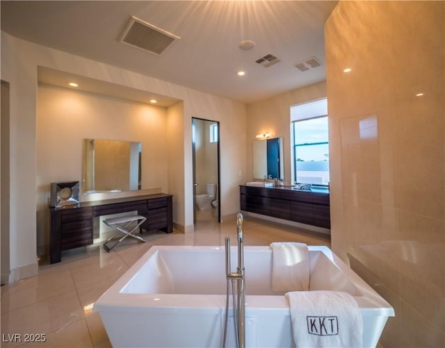 bathroom with toilet, a freestanding tub, visible vents, and vanity