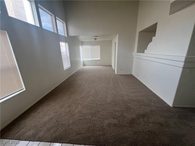 carpeted empty room featuring a towering ceiling and baseboards