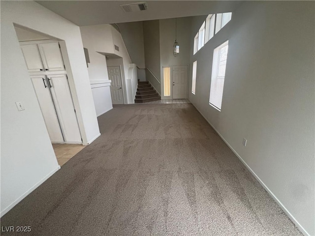 unfurnished living room with visible vents, a towering ceiling, light carpet, baseboards, and stairs