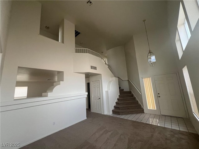 tiled foyer with carpet, visible vents, stairway, and a towering ceiling