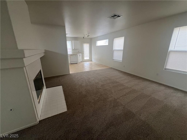 unfurnished living room with light carpet, a tiled fireplace, visible vents, and baseboards