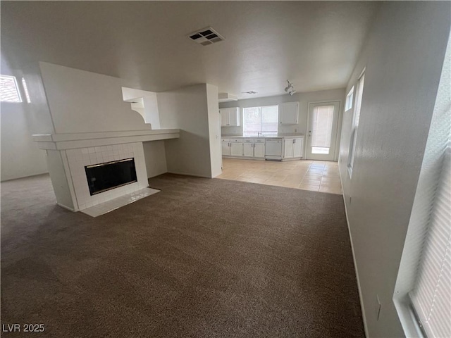 unfurnished living room featuring light colored carpet, visible vents, a tiled fireplace, and light tile patterned flooring