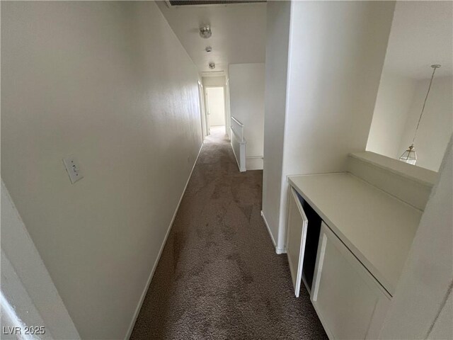 hall featuring baseboards and dark carpet