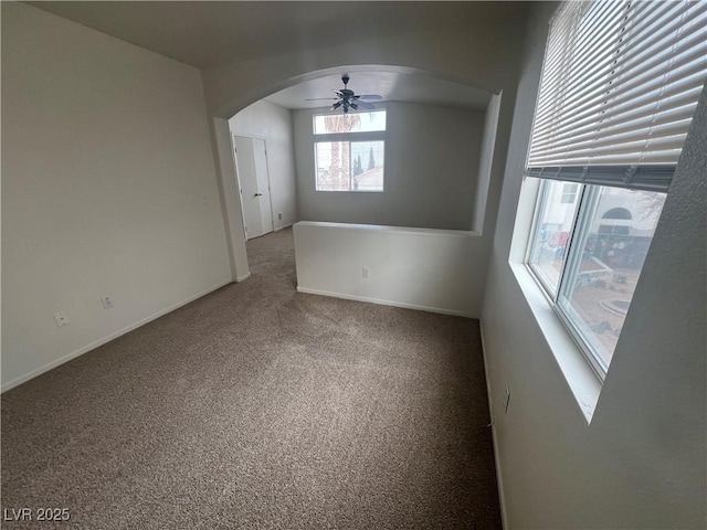 empty room with a ceiling fan, arched walkways, carpet flooring, and baseboards