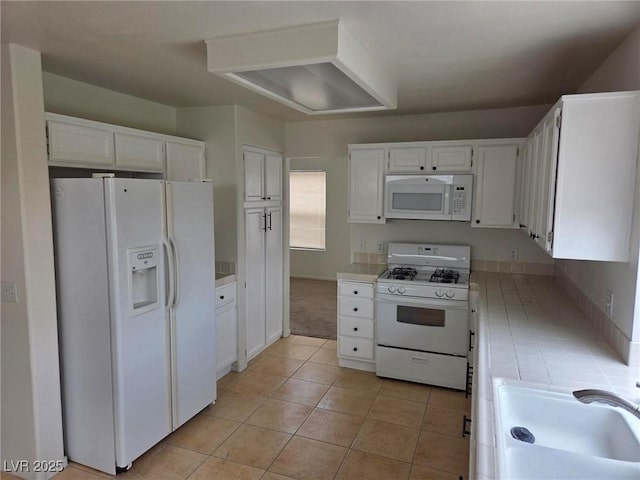 kitchen with white appliances, white cabinetry, a sink, and light tile patterned floors