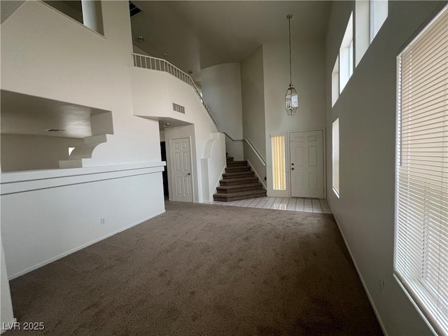 unfurnished living room featuring stairway, carpet flooring, visible vents, and a healthy amount of sunlight