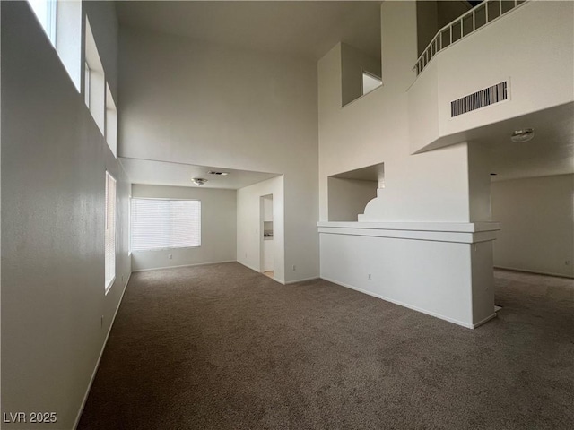 spare room featuring a towering ceiling, baseboards, visible vents, and carpet flooring