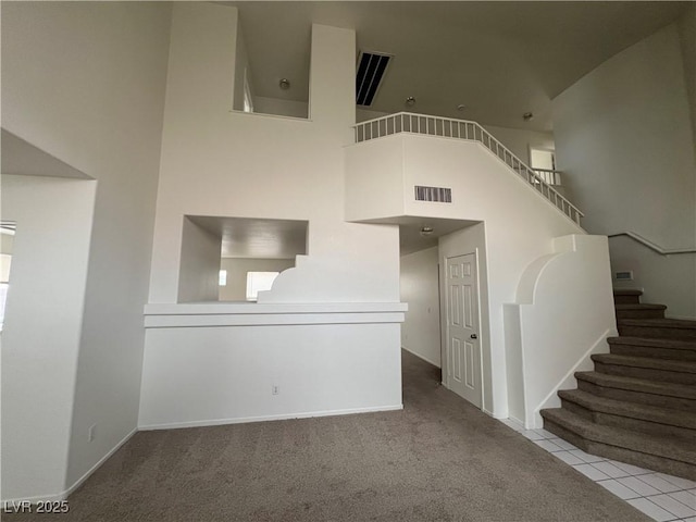 interior space with baseboards, visible vents, a high ceiling, and stairs