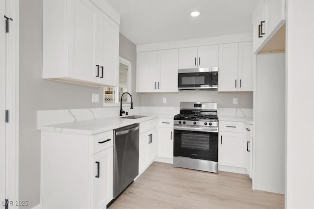 kitchen featuring light wood finished floors, stainless steel appliances, white cabinets, a sink, and light stone countertops