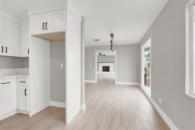 kitchen with light countertops, a brick fireplace, light wood-style flooring, and white cabinets