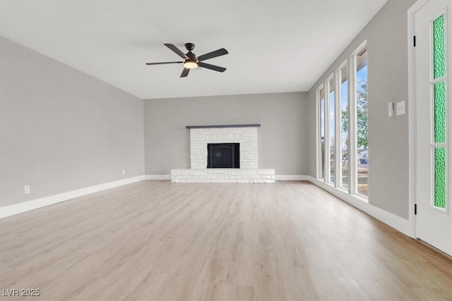 unfurnished living room featuring a ceiling fan, a brick fireplace, baseboards, and light wood finished floors