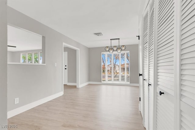 unfurnished dining area with light wood-style floors, visible vents, baseboards, and an inviting chandelier