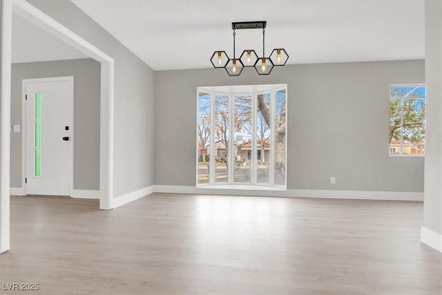 unfurnished dining area with baseboards, an inviting chandelier, and wood finished floors