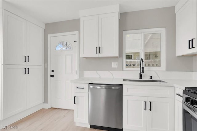 kitchen with white cabinets, light wood-style flooring, light stone countertops, stainless steel dishwasher, and a sink