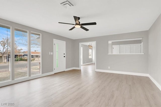 empty room featuring ceiling fan with notable chandelier, wood finished floors, visible vents, and baseboards