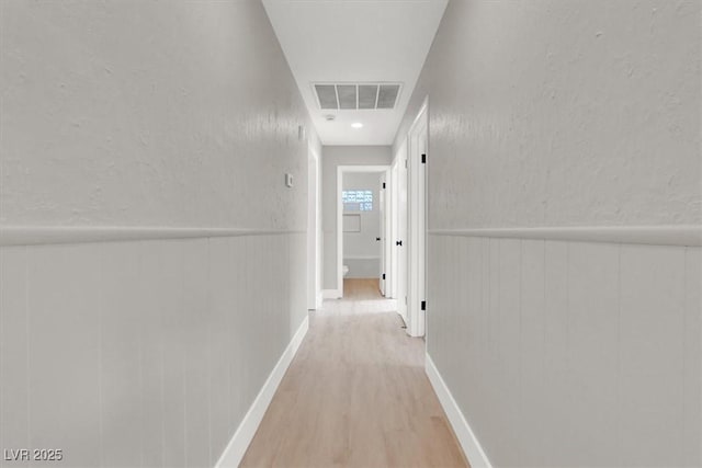 hall featuring a textured wall, wainscoting, wood finished floors, and visible vents