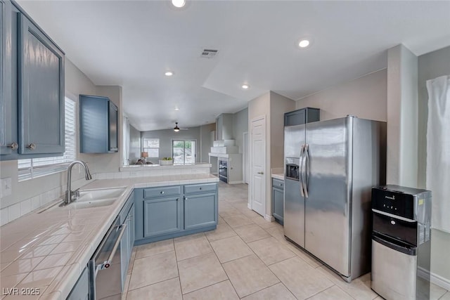 kitchen featuring visible vents, tile countertops, appliances with stainless steel finishes, a peninsula, and a sink