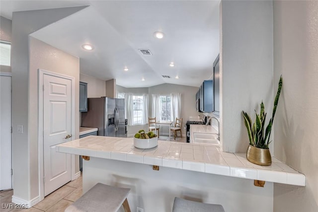 kitchen featuring visible vents, a breakfast bar, a peninsula, stainless steel refrigerator with ice dispenser, and a sink